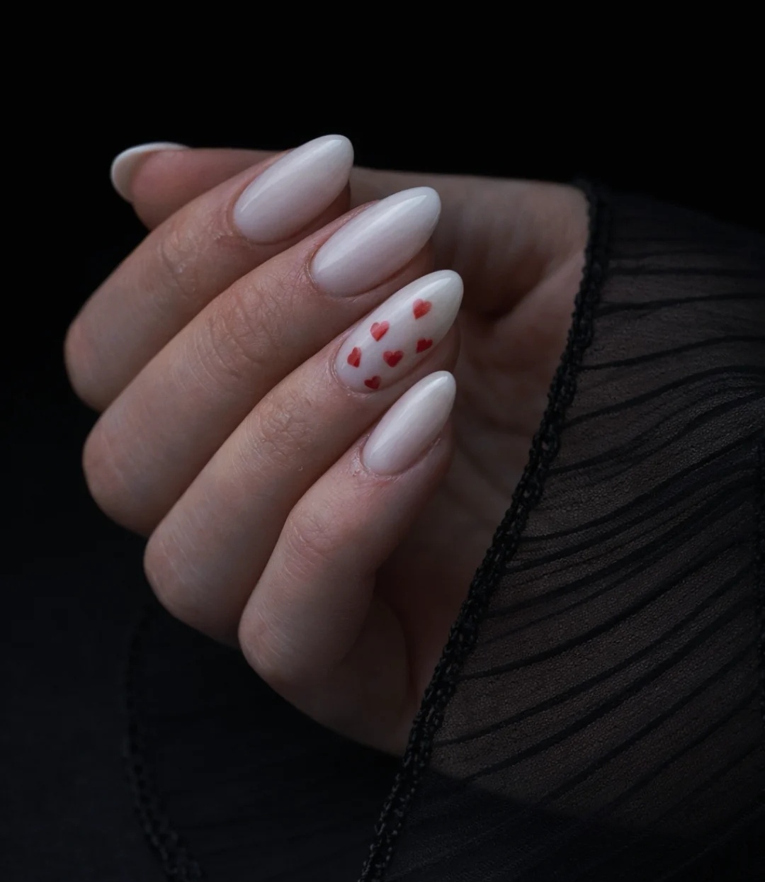 Ongles en amande nude avec un nail art délicat de petits cœurs rouges, réalisé à Zimmerbach.