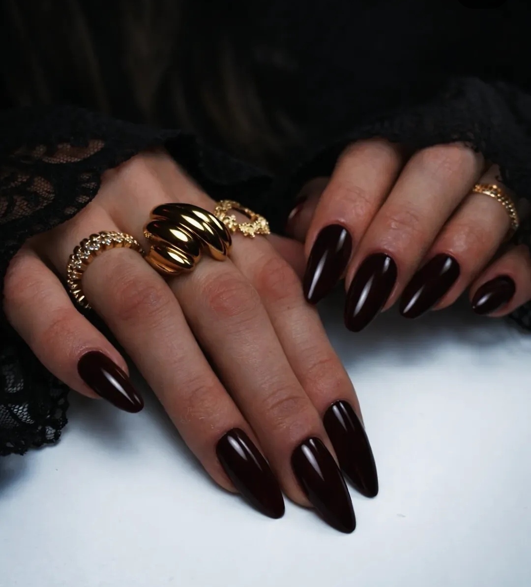 Ongles longs en amande dans une teinte bordeaux foncé, une pose élégante aux reflets brillants réalisée à Zimmerbach.